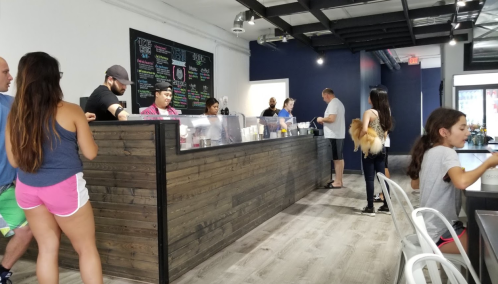 A busy café with customers at the counter and seating areas, featuring a menu board on the wall.
