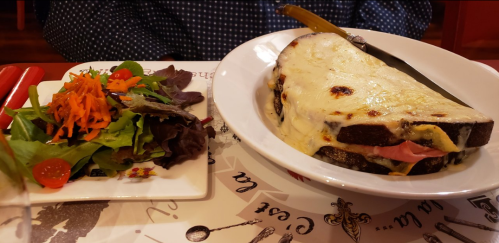 A plate with a large cheesy sandwich and a side salad with mixed greens, carrots, and cherry tomatoes.