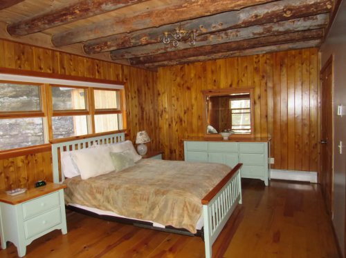 Cozy bedroom with wooden walls, a bed, dresser, and large windows letting in natural light.