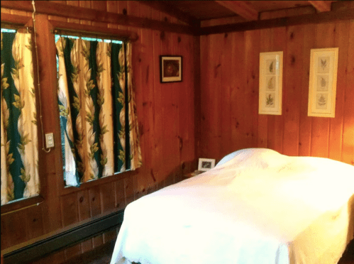 Cozy wooden bedroom with a bed, patterned curtains, and framed artwork on the walls. Warm, inviting atmosphere.