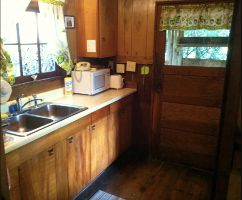 Cozy kitchen with wooden cabinets, a sink, microwave, and a door leading outside, featuring floral curtains.