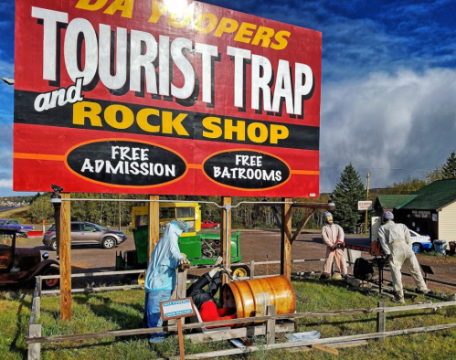 A colorful sign for "Da Yoopers Tourist Trap and Rock Shop" with people working nearby and a vintage vehicle in the background.