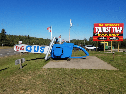 A large blue airplane sculpture named "Big Gus" next to a colorful sign for a tourist trap and rock shop.