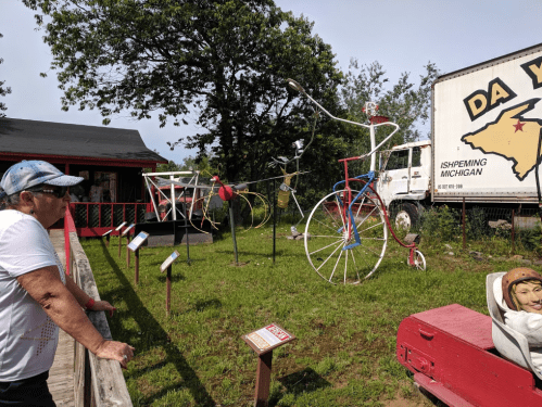 A person observes large, colorful bicycle sculptures in a grassy area near a building and a truck.