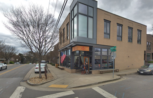 A corner building with large windows, an American flag, and people outside on a cloudy day.