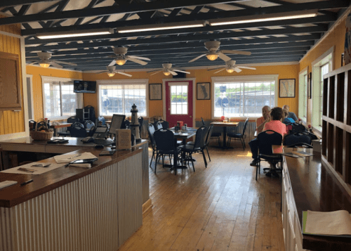 A bright, casual dining area with wooden floors, ceiling fans, and tables occupied by patrons.