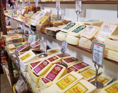 A display of various cheeses on shelves, each labeled with colorful packaging and price tags.