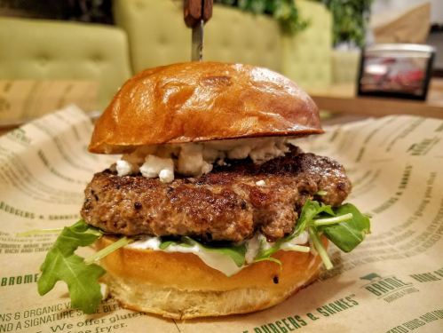 A juicy burger with a beef patty, lettuce, and creamy sauce, served on a toasted bun with a toothpick on top.
