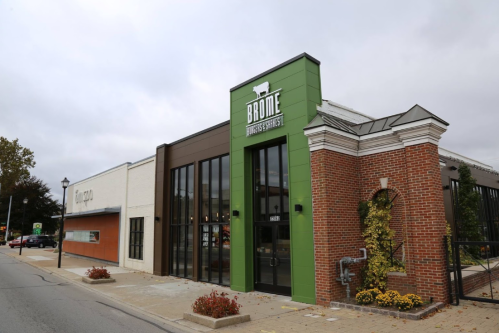 Exterior of a modern building with a green and brick facade, featuring the sign "Brome" and decorative plants.