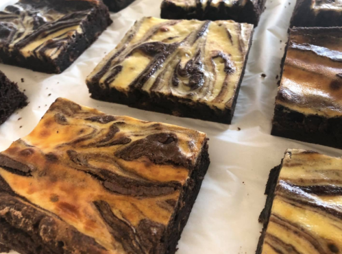 A close-up of swirled cheesecake brownies on a white surface, showcasing rich chocolate and creamy layers.
