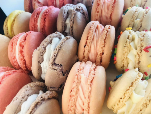 A colorful assortment of macarons in various flavors, featuring pink, beige, and pastel colors with cream fillings.
