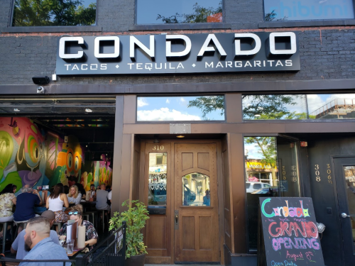 Exterior of Condado Tacos restaurant featuring a colorful mural and a sign announcing "Grand Opening."