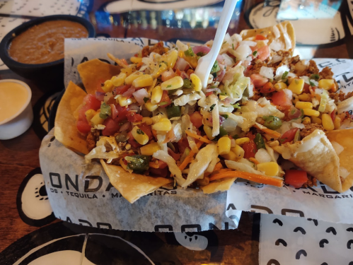 A plate of nachos topped with vegetables, cheese, and meat, served with sides of salsa and sauce.