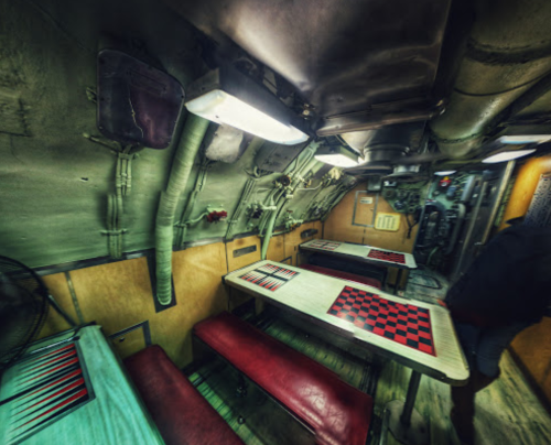 Interior of a submarine with tables and benches, featuring red and black checkered patterns, and industrial walls.