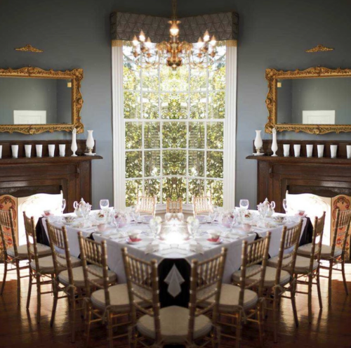 Elegant dining room with a mirrored table setting, large windows, and ornate decor, creating a sophisticated atmosphere.