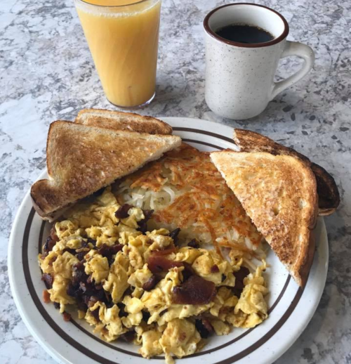 A plate with scrambled eggs, hash browns, and toast, accompanied by a glass of orange juice and a cup of coffee.