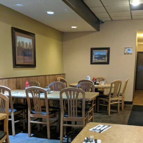 Cozy restaurant interior with wooden tables and chairs, framed artwork, and condiments on the tables.
