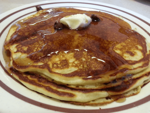 A stack of golden pancakes topped with a pat of butter and drizzled with syrup on a plate.