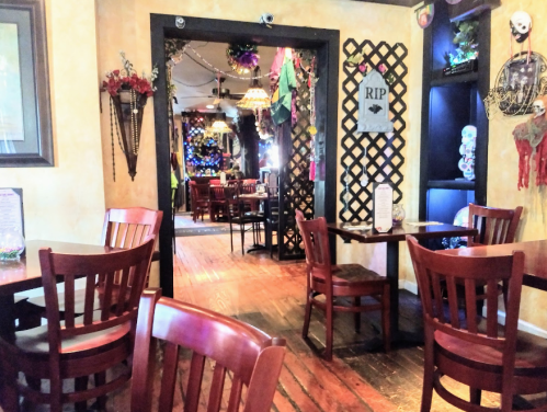 Interior of a restaurant featuring wooden tables, chairs, and festive decorations, with a view into a decorated area.