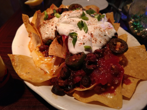 A plate of nachos topped with cheese, jalapeños, olives, salsa, sour cream, and green onions.