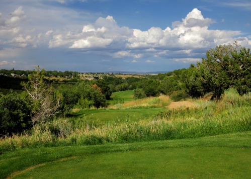 A scenic view of a golf course surrounded by lush greenery and rolling hills under a partly cloudy sky.