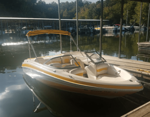 A white and yellow boat docked at a marina, surrounded by calm water and trees in the background.