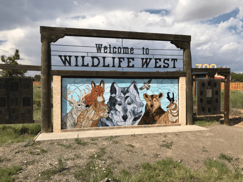 Sign for Wildlife West featuring a colorful mural of various animals, set against a cloudy sky.