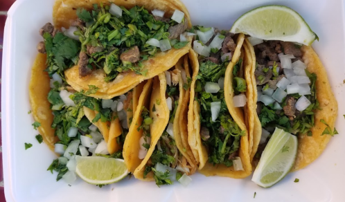 A plate of tacos filled with meat, topped with chopped onions and cilantro, served with lime wedges.