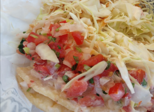 A close-up of tacos topped with fresh pico de gallo and shredded cabbage on a white plate.