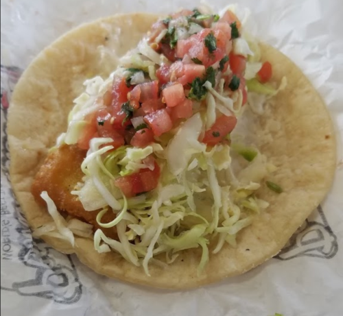 A taco filled with crispy fish, shredded lettuce, and fresh tomato salsa on a soft tortilla.
