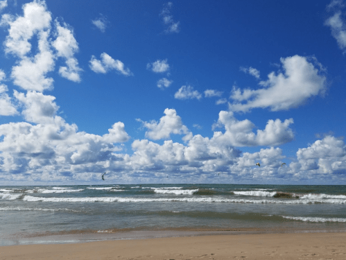 A sunny beach scene with waves, a blue sky, and fluffy white clouds scattered above.