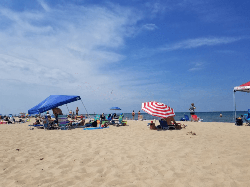 A sunny beach scene with people relaxing under colorful umbrellas on the sand, with the ocean in the background.
