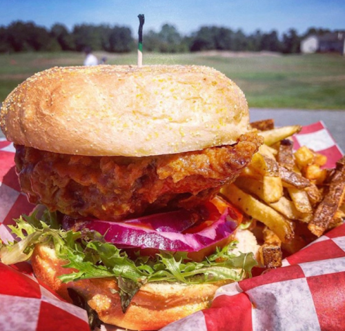 A crispy fried chicken sandwich with lettuce, onion, and fries, served in a red and white checkered basket.