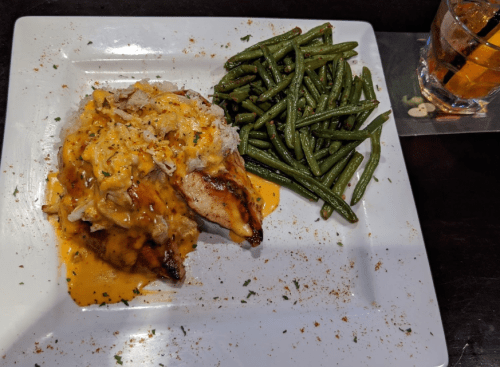 Grilled chicken topped with cheese sauce, served with rice and green beans on a white plate.