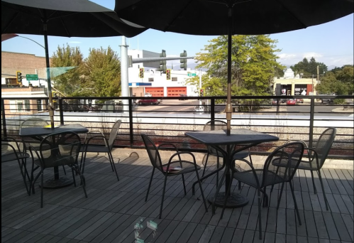 Outdoor seating area with empty tables under umbrellas, overlooking a street with traffic lights and nearby buildings.