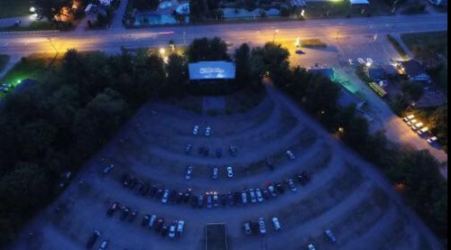 Aerial view of a drive-in theater with parked cars and illuminated surroundings at night.
