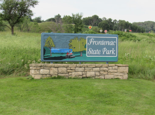 Sign for Frontenac State Park featuring a scenic illustration and stone base, surrounded by green grass and trees.