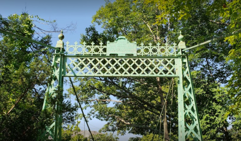 Green decorative bridge structure surrounded by trees, featuring a lattice design and an inscription at the top.