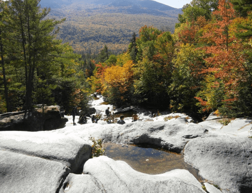 A scenic view of a rocky stream surrounded by vibrant autumn foliage and people exploring the area.