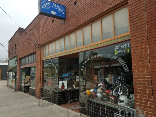 Exterior of Time Warp Tea Room, featuring large windows displaying helmets and vintage items, with a sign above.