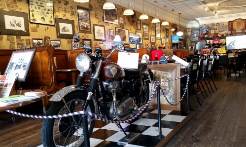 A vintage motorcycle displayed in a retro-themed café with historical photos and memorabilia on the walls.