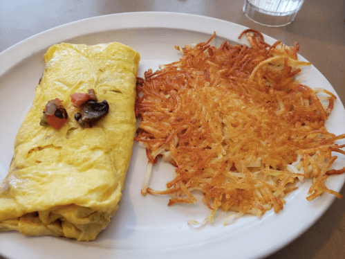 A plate featuring a fluffy omelet with vegetables and a side of crispy golden hash browns.