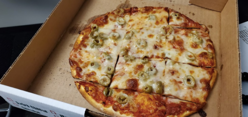 A pizza with melted cheese and green olives, cut into slices, in a cardboard pizza box.