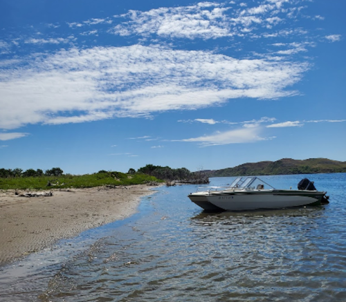 A boat anchored on a sandy beach with clear blue skies and gentle waves in the background.