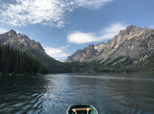 A serene lake surrounded by mountains and lush forests under a blue sky with scattered clouds.