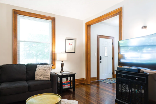 Cozy living room with a black couch, lamp, TV, and wooden accents, featuring a door leading outside.