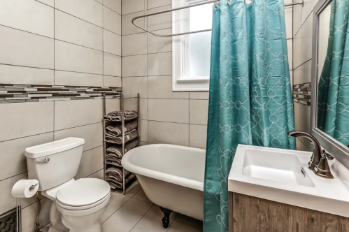 A modern bathroom featuring a bathtub, toilet, sink, and a turquoise shower curtain with neatly stacked towels.
