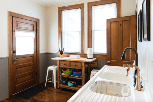 Bright kitchen with wooden accents, a sink, a countertop with colorful bowls, and a door leading outside.