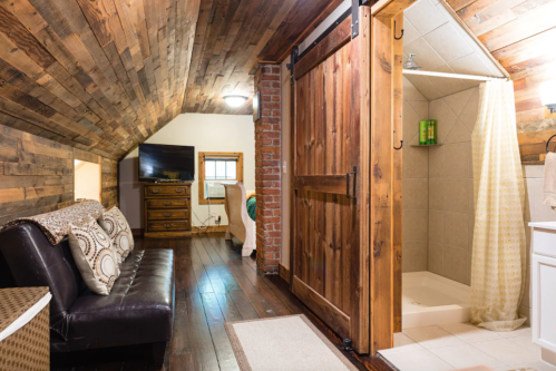 Cozy attic space with wooden ceiling, a sofa, and a bathroom featuring a shower and rustic sliding door.