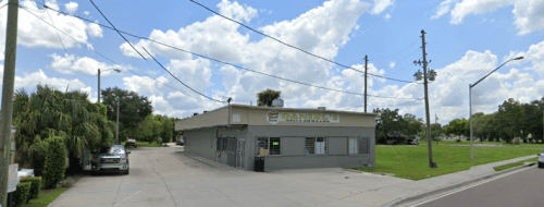 A small, single-story building with a sign reading "Daniello's" surrounded by trees and power lines under a cloudy sky.